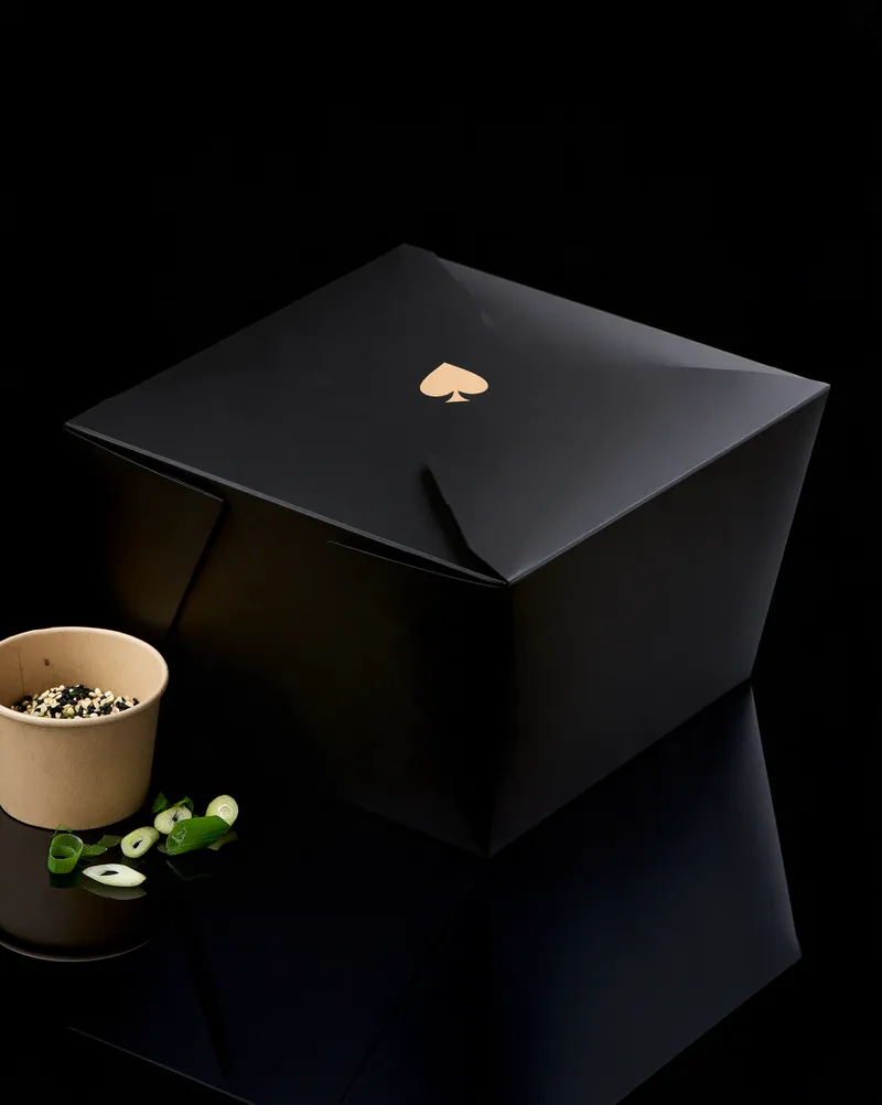 The Jackpot Wings black folded fiber box, closed, with a small gold spade mark and a compostable garnish cup.